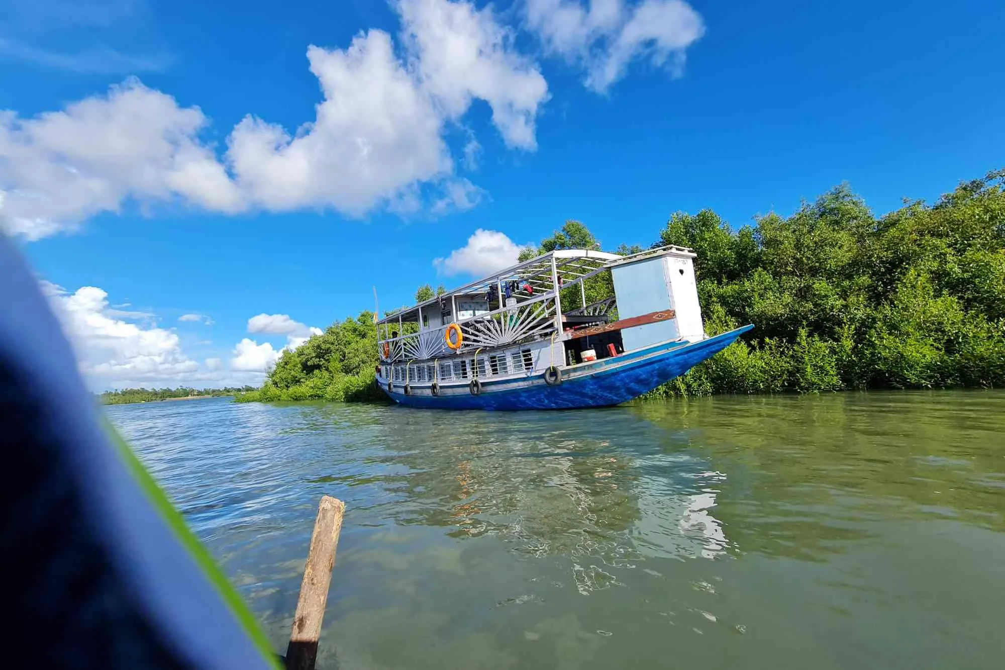Big launch boat in Sundarbans river with mangrove forest, clear sky, and blue-colored launch.