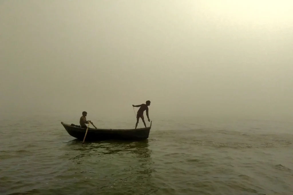 Two Sundarban kids catching fish from small wooden boat in river